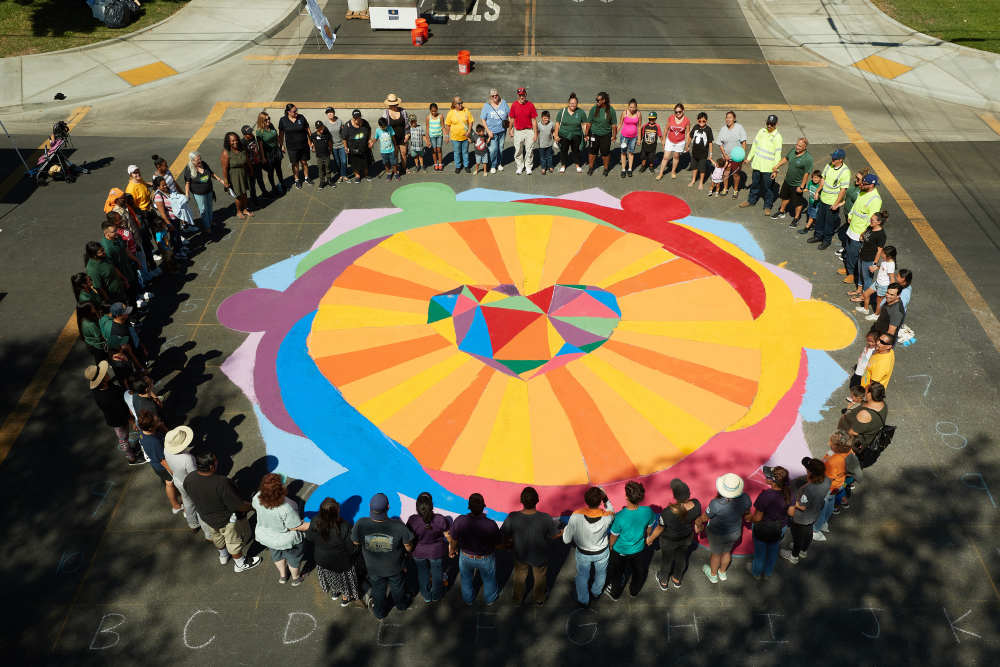 People circle up around a large outdoor painting in the middle of an intersection