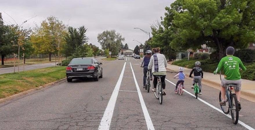 Photo of adults and children riding bicycles in a buffered bike lane on a street with a median